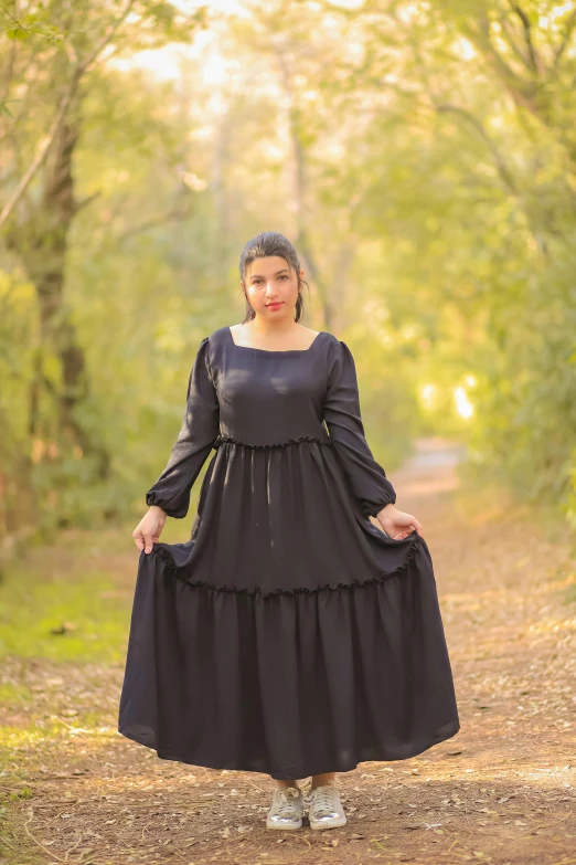 the woman in a black dress poses on a dirt road