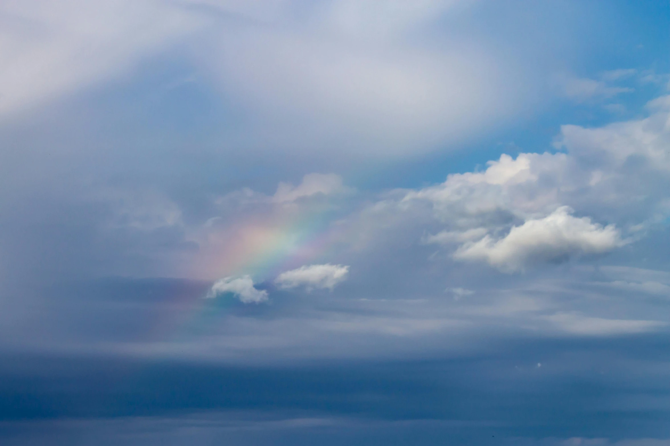 a rainbow appears over the ocean under the cloudy sky