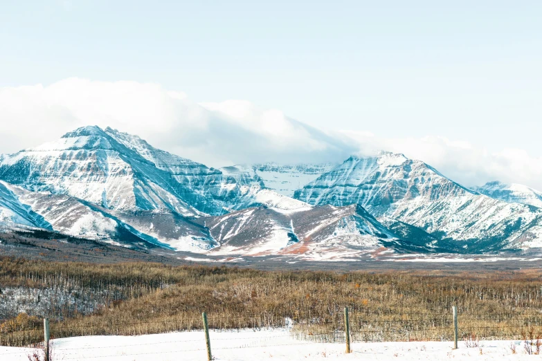 mountains and snow covers a large field near a fence