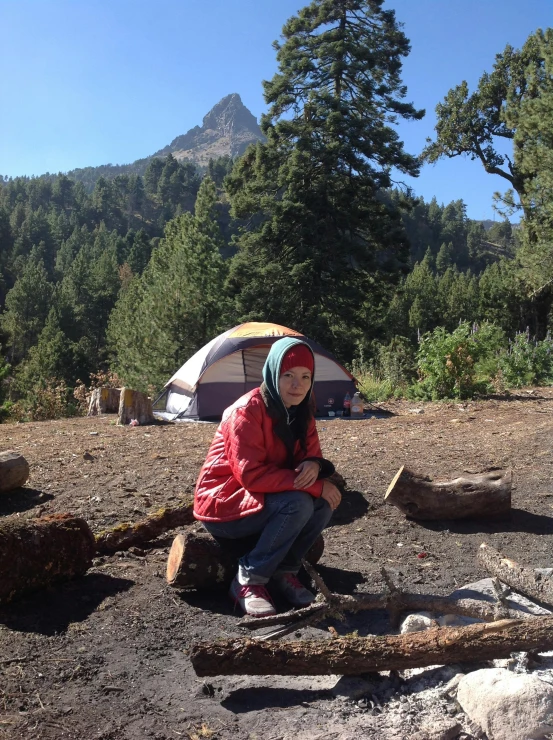 the woman sits with her camping equipment and looks at her cell phone