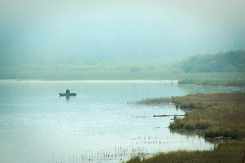 a person is fishing in a lake with fog