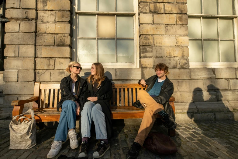 three people are sitting on a bench outside a large building