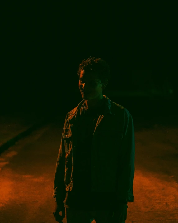 a person wearing a dark blue jacket and a green shirt standing in a dimly lit area