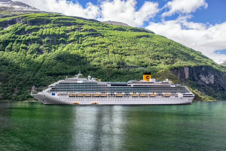 cruise ship sailing down the ocean in front of a mountain