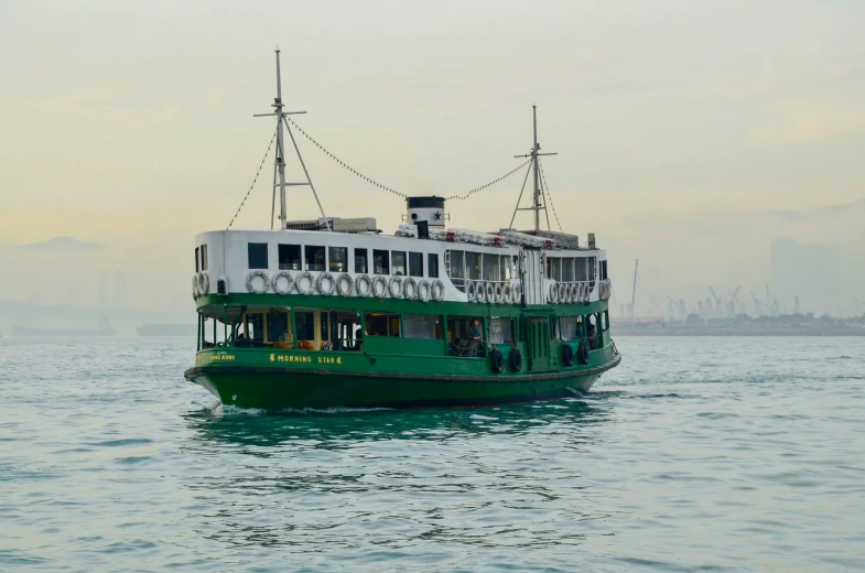 a green and white boat in the water with an island behind it