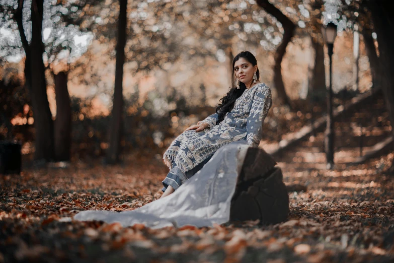 a woman sitting on top of a fallen leaf covered park