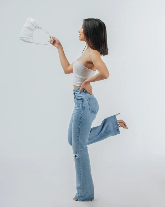 a woman in high - rise jeans poses while holding a fan