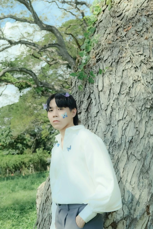 an asian girl with freckles leans against a tree