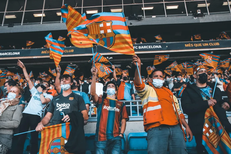 several people at an event wearing orange, blue and black striped scarfs and face masks and waving flags