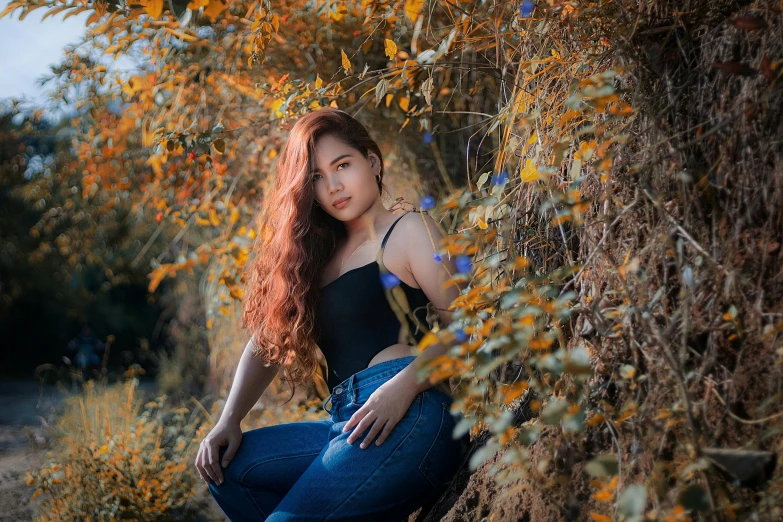 a woman squats beneath a tree and looks at the camera