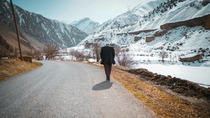 a man walks along an empty road, towards snowy mountains