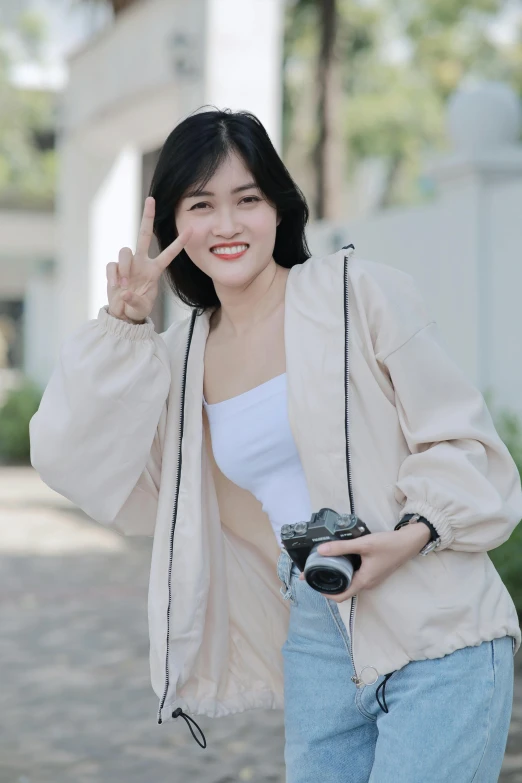 a young asian woman holding a camera making the number one gesture