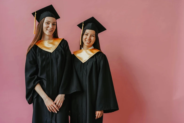 two people dressed up and standing against a wall wearing caps and gowns