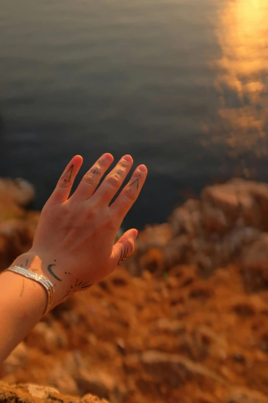 someone's hand with some writing on it sitting near a body of water