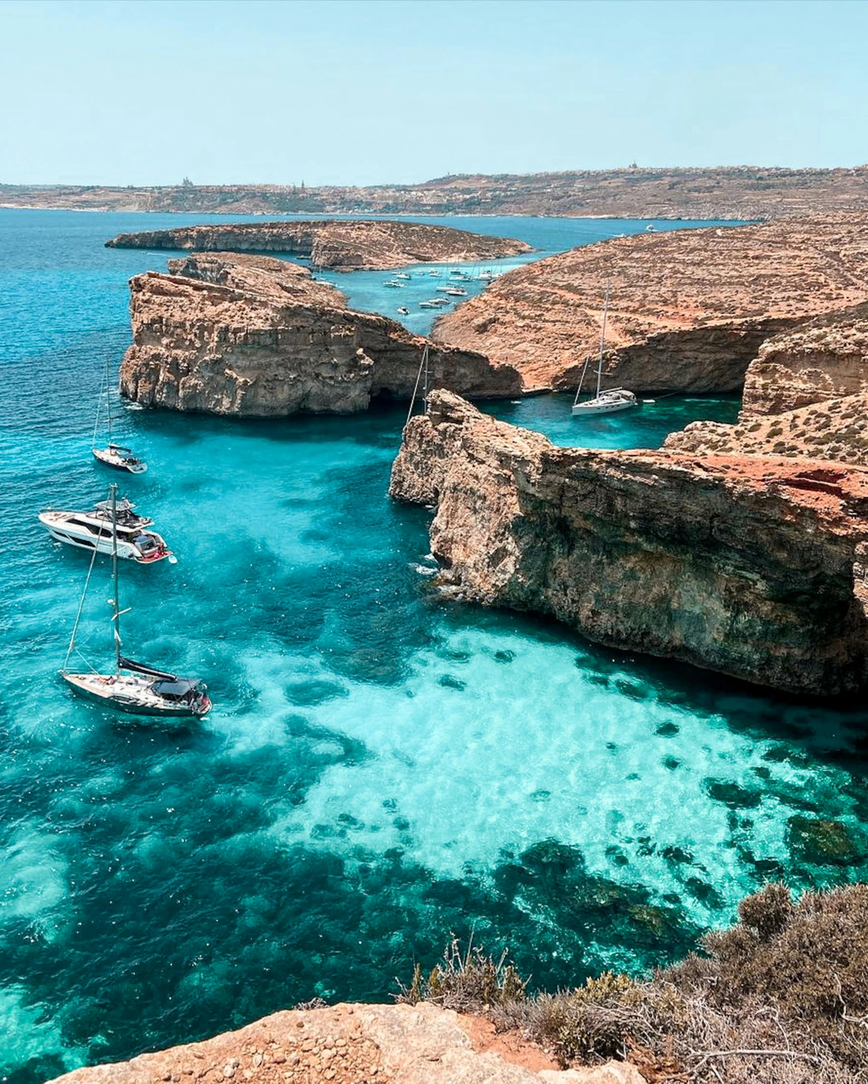 boats float through an ocean between cliffs