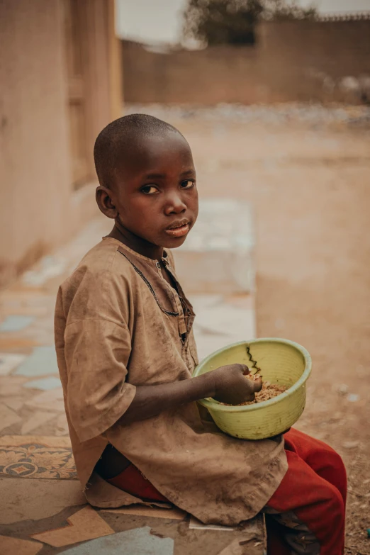 a boy sits with a bowl of food in his lap