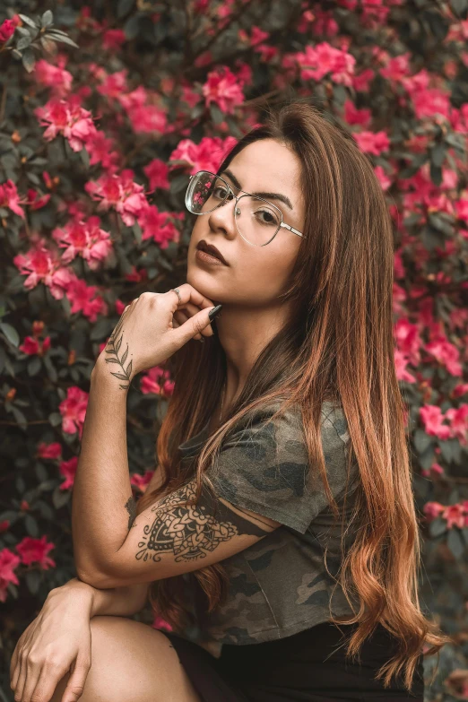 a young woman poses by pink flowers wearing glasses