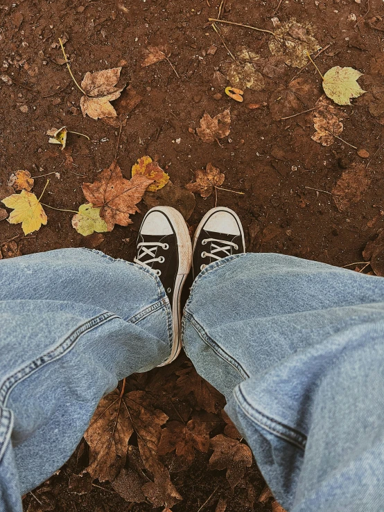 someone wearing white tennis shoes standing on an area with leaves