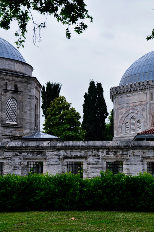 two large, domed stone buildings are standing behind hedge