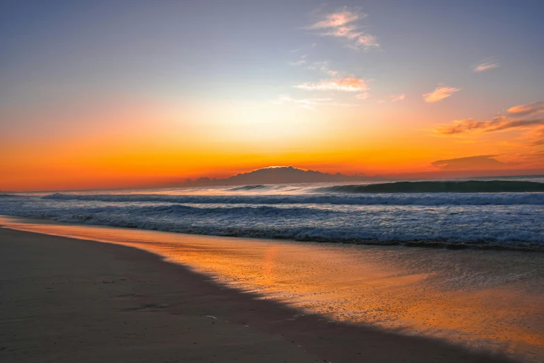 an ocean shore with waves in the sunset and a mountain in the distance