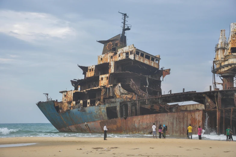 people are walking around on the beach near a rusted ship