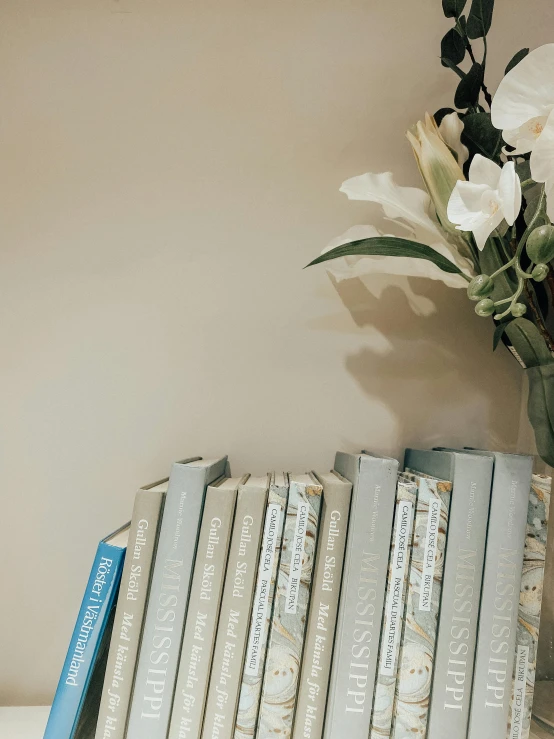a shelf with several books on it next to a vase of flowers