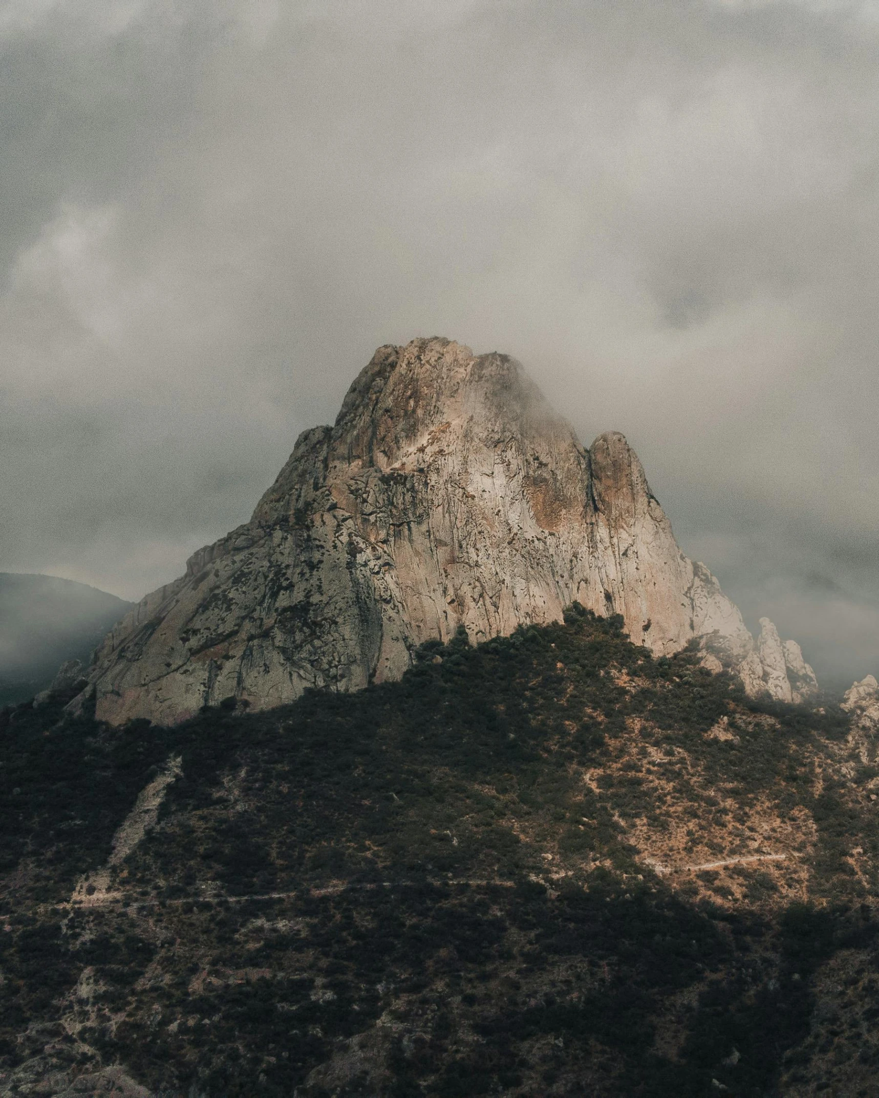 two mountain ranges under a cloudy sky with some trees in front