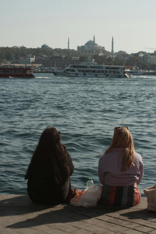 two girls sitting on the dock overlooking some water