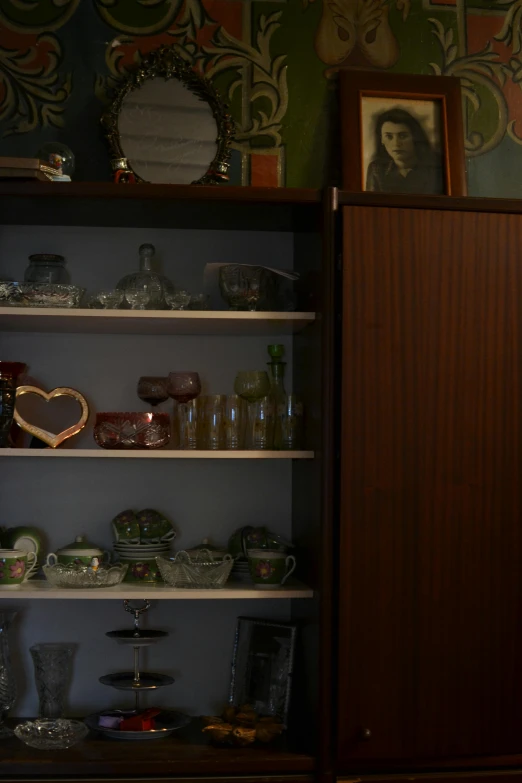 a brown wooden shelf filled with glassware next to a wall painting