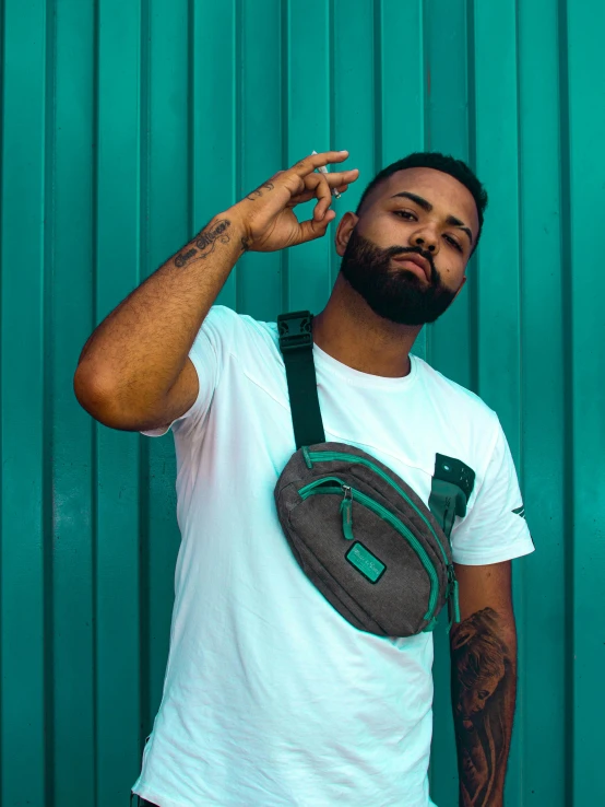 a man standing near a blue wall with a green hand bag