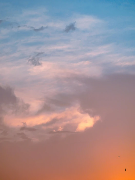 a plane flies in the cloudy sky at sunset