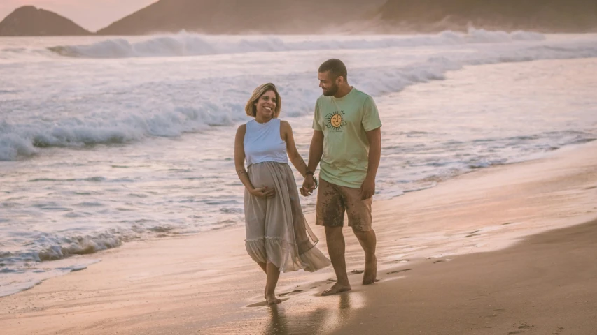 a young man holding the hands of a woman while standing on the beach