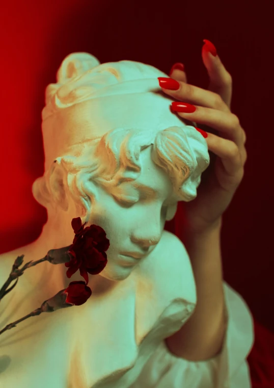 a statue of a woman in a white dress with red nails holding her face to her head