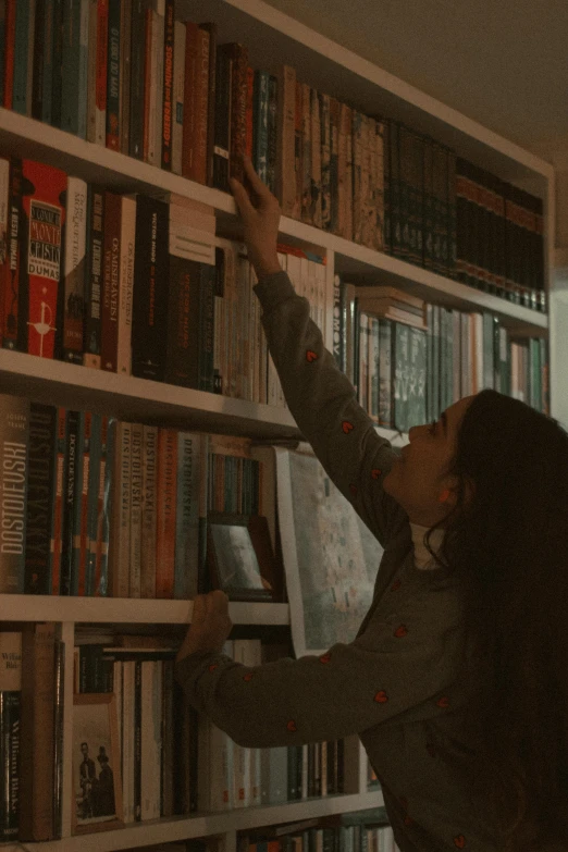 a person reaching up to the wall with books on it