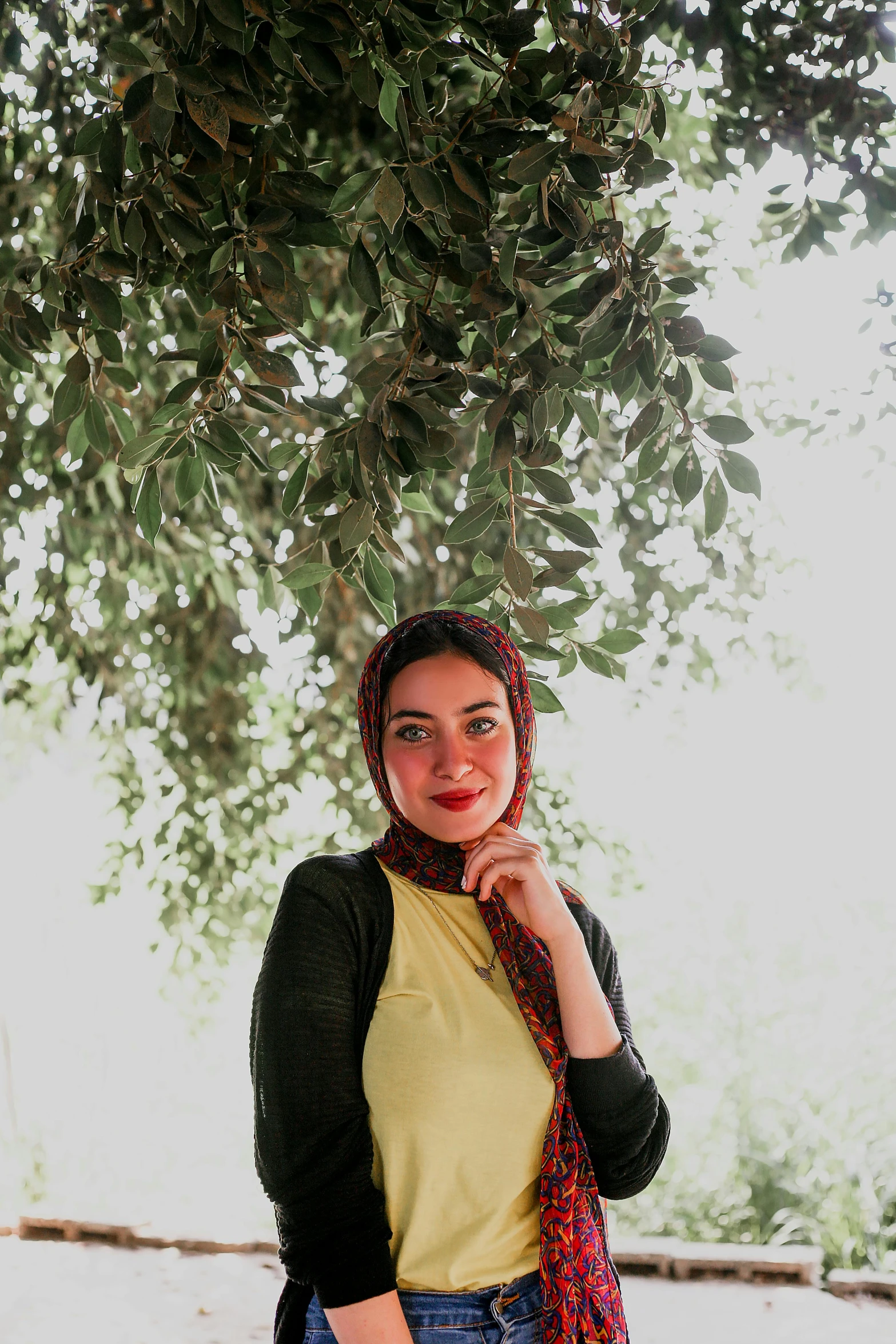 a woman standing under a tree in a yellow shirt and scarf