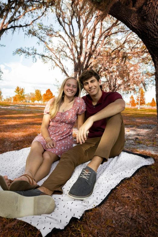 a man and woman on a blanket under a tree