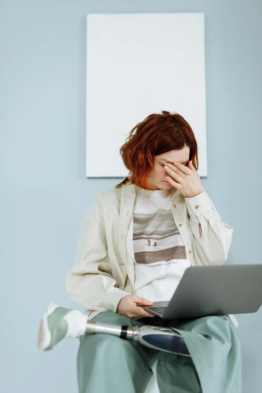 a woman holding her face to her hands and looking at a computer