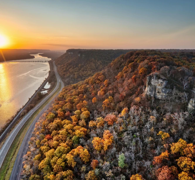 the sun sets behind a valley near a highway