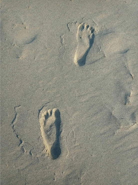 two footprints are left in the sand next to a car