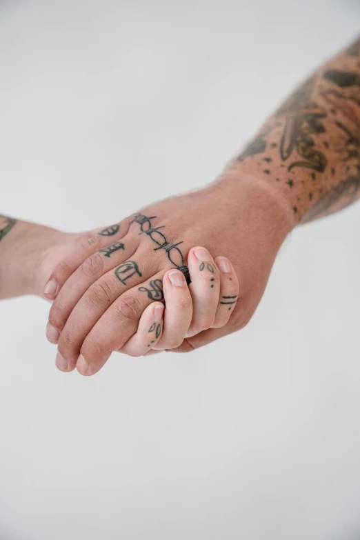 two people holding hands with tattoos on their arms