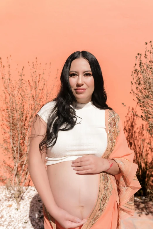 pregnant woman standing on a pink background with her arms around her belly