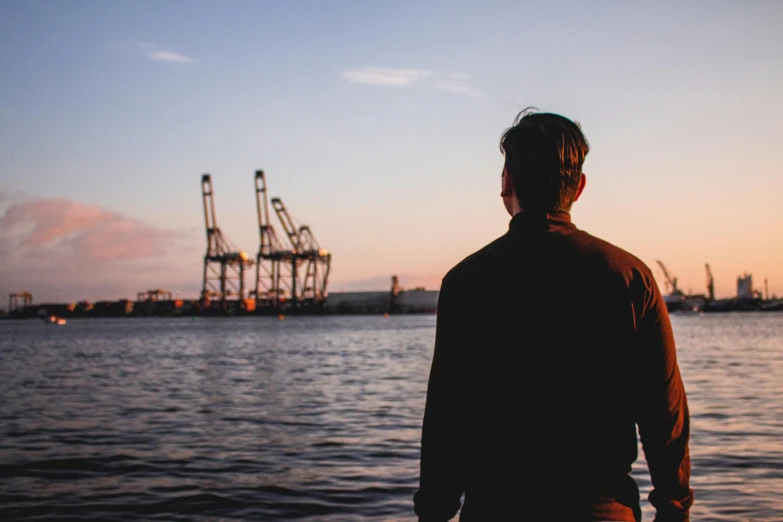 man standing near the water looking at cranes