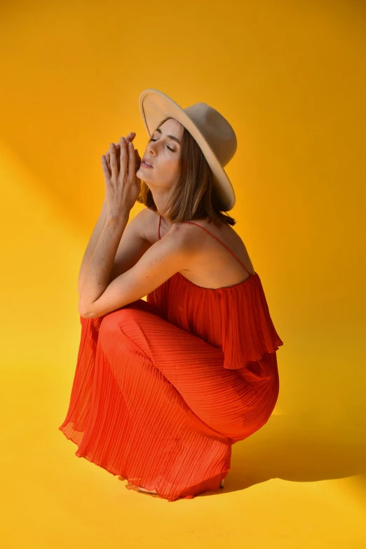 a woman wearing a straw hat poses with her hands clasped