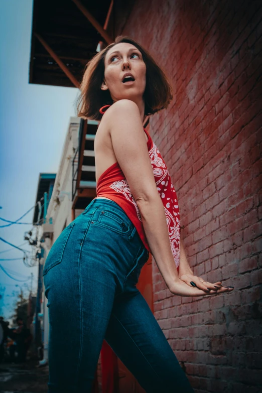 a woman leaning against a red brick building, with her arm extended forward