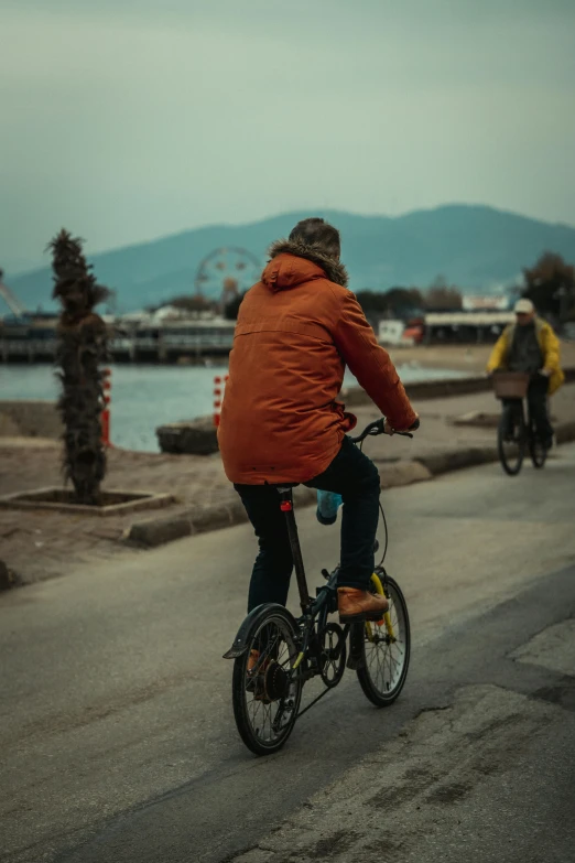 two bicyclists ride near the ocean side on a cloudy day