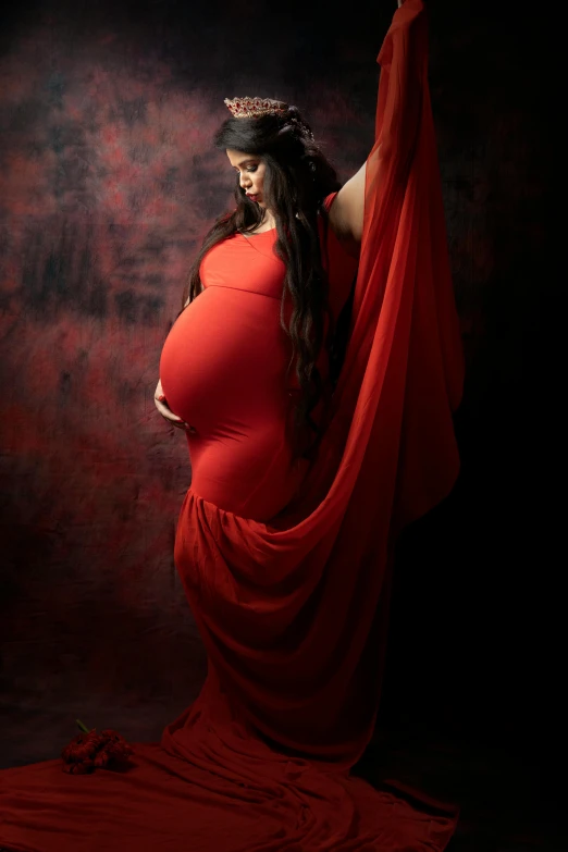 a pregnant belly girl dressed in a red gown and tiara