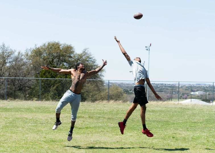 two men leaping to catch a football in a park