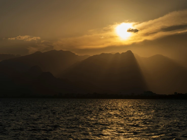 a lake surrounded by hills with the sun shining through