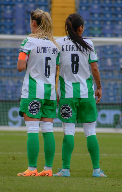 two girls on soccer uniforms look on with delight
