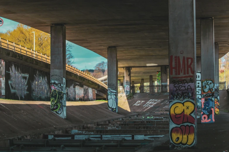 a skate park with many ramps and graffiti under a bridge